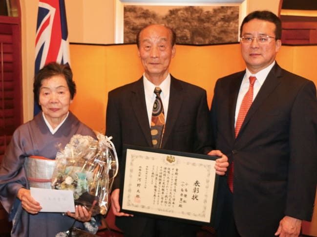 田中一成･ブリスベン総領事（右）より表彰状を受け取った小島氏（中央）と妻･文子さん（同左）（Photo：Taka Uematsu）